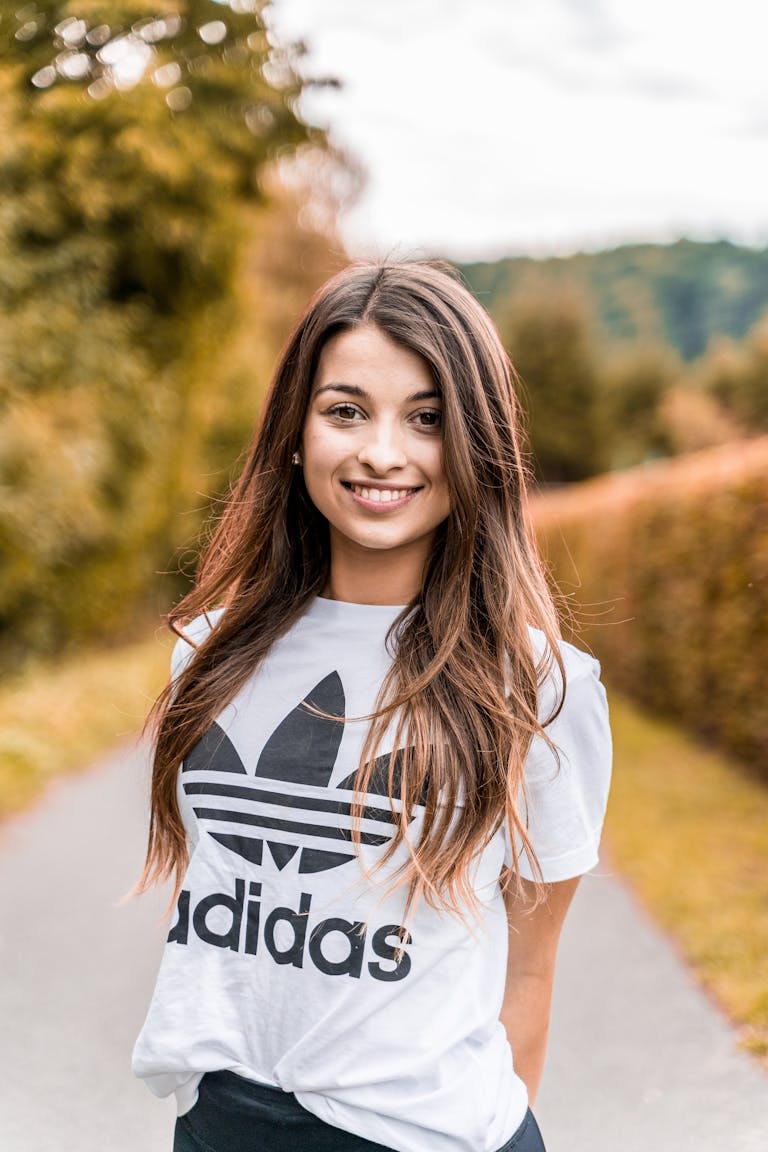 Young woman smiling in a white shirt with logo, posing outdoors.