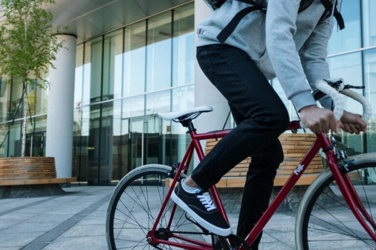 A cyclist in black jeans rides a red bike quickly through an urban area, showcasing fast urban transport.