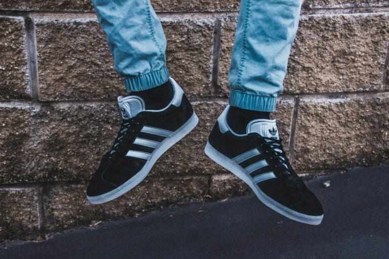 Close-up shot of Adidas sneakers and denim jeans against a brick wall, showcasing urban street style.