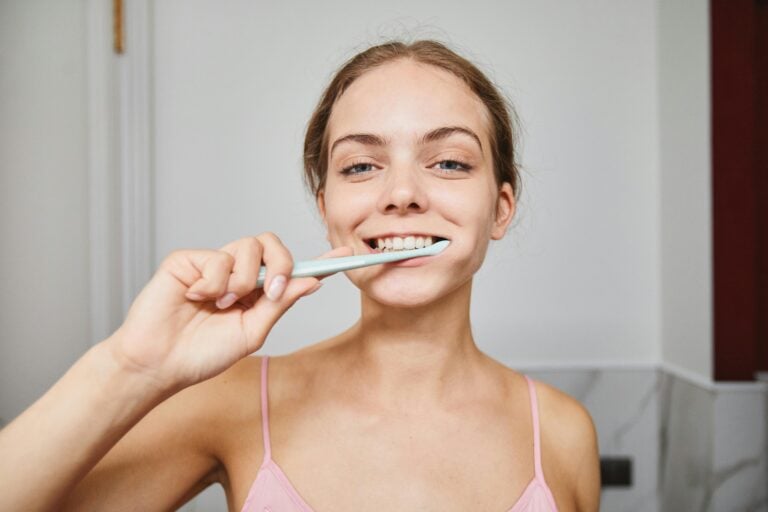 Close-up of a woman smiling while brushing teeth in a modern bathroom.