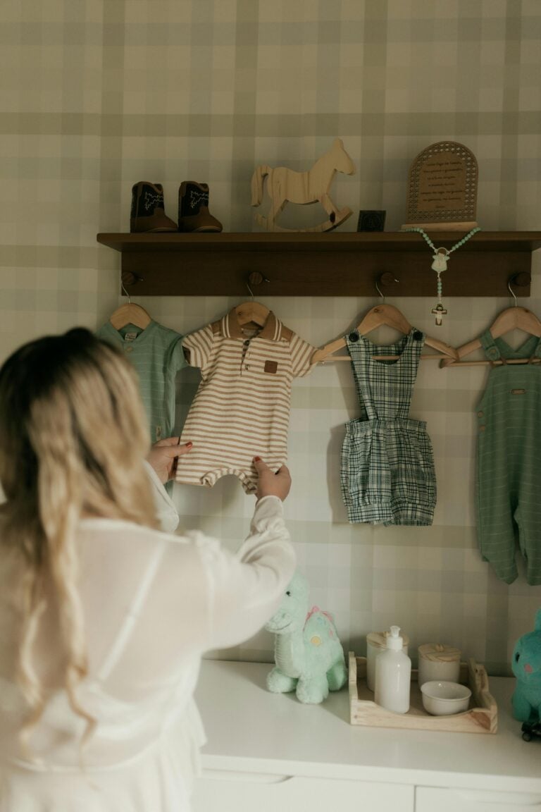 A mother is selecting baby clothes from a shelf in a softly lit nursery room.