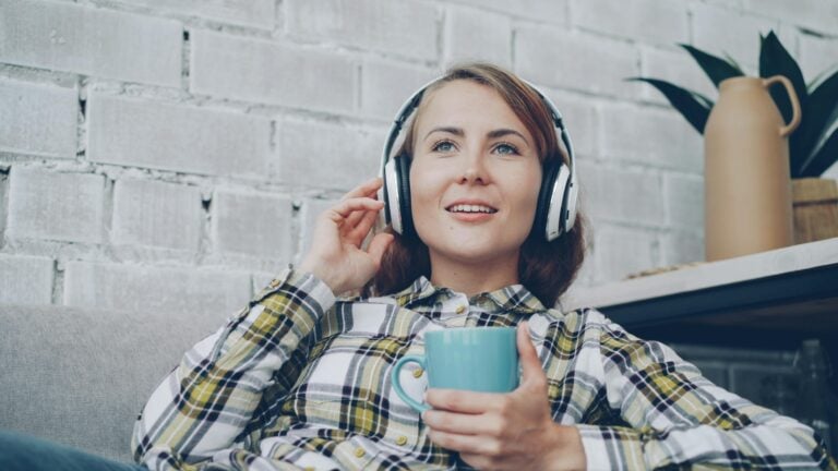 Smiling woman with headphones and coffee, relaxing indoors. Cozy listening experience.