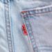 Detailed close-up of light blue denim jeans featuring a red tag on the seam.