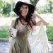 Cheerful woman in a boho dress with a camera enjoying a sunny day outdoors.