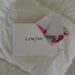 Top view of Lancome gift box and floral envelope on a white bed.