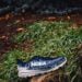 Outdoor trail running shoe resting on a rock surrounded by lush greenery.