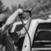 Black and white image of a man using a power spray on a truck outdoors.