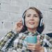 Smiling woman with headphones and coffee, relaxing indoors. Cozy listening experience.