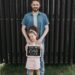 A joyful father and daughter sharing a bonding moment with a touching handwritten sign outdoors.